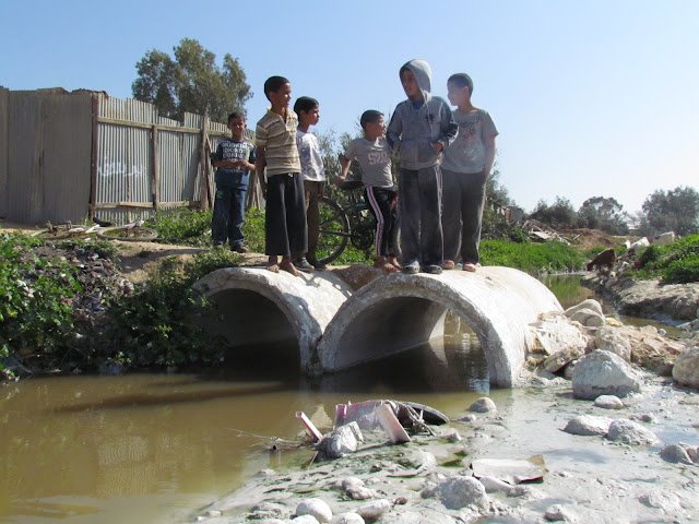 أطفال قرية أم بطين فوق نهر المياه العادمة الذي يمر وسط قريتهم